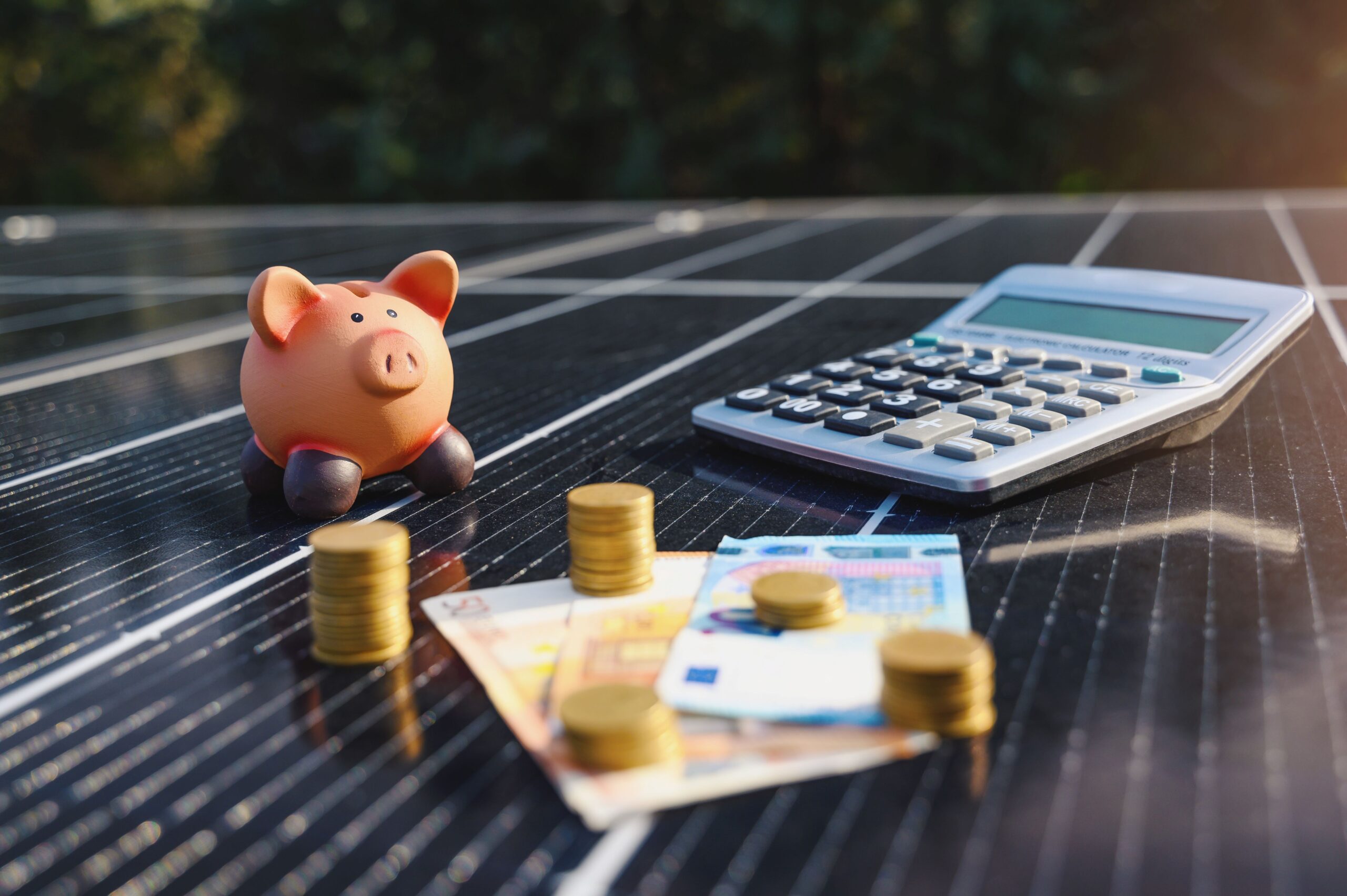 Auf einer Solaranlage liegen Geld, ein Sparschwein und ein Taschenrechner 